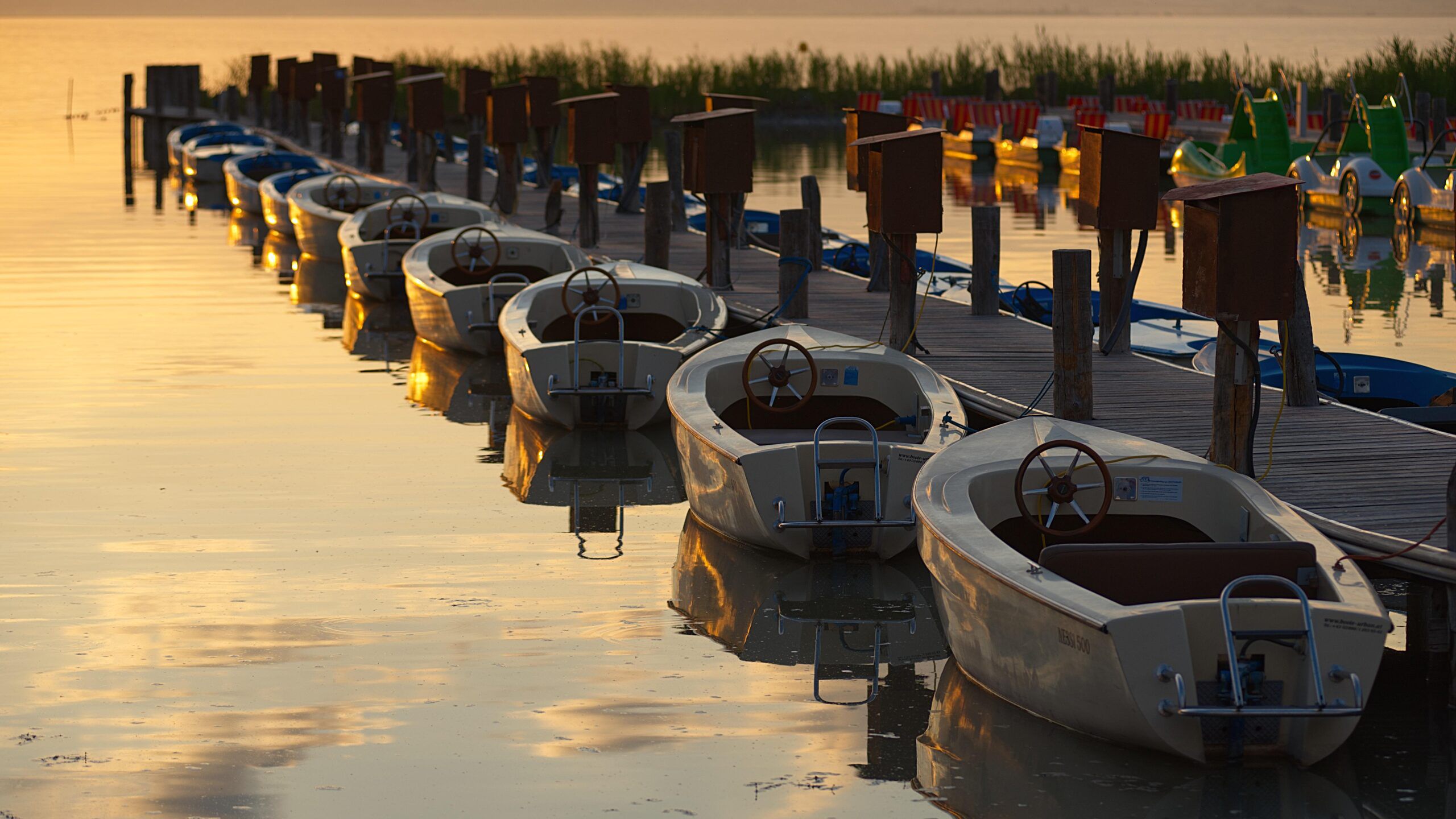 Electric boats moored along a wooden jetty on Lake Fertő at sunset