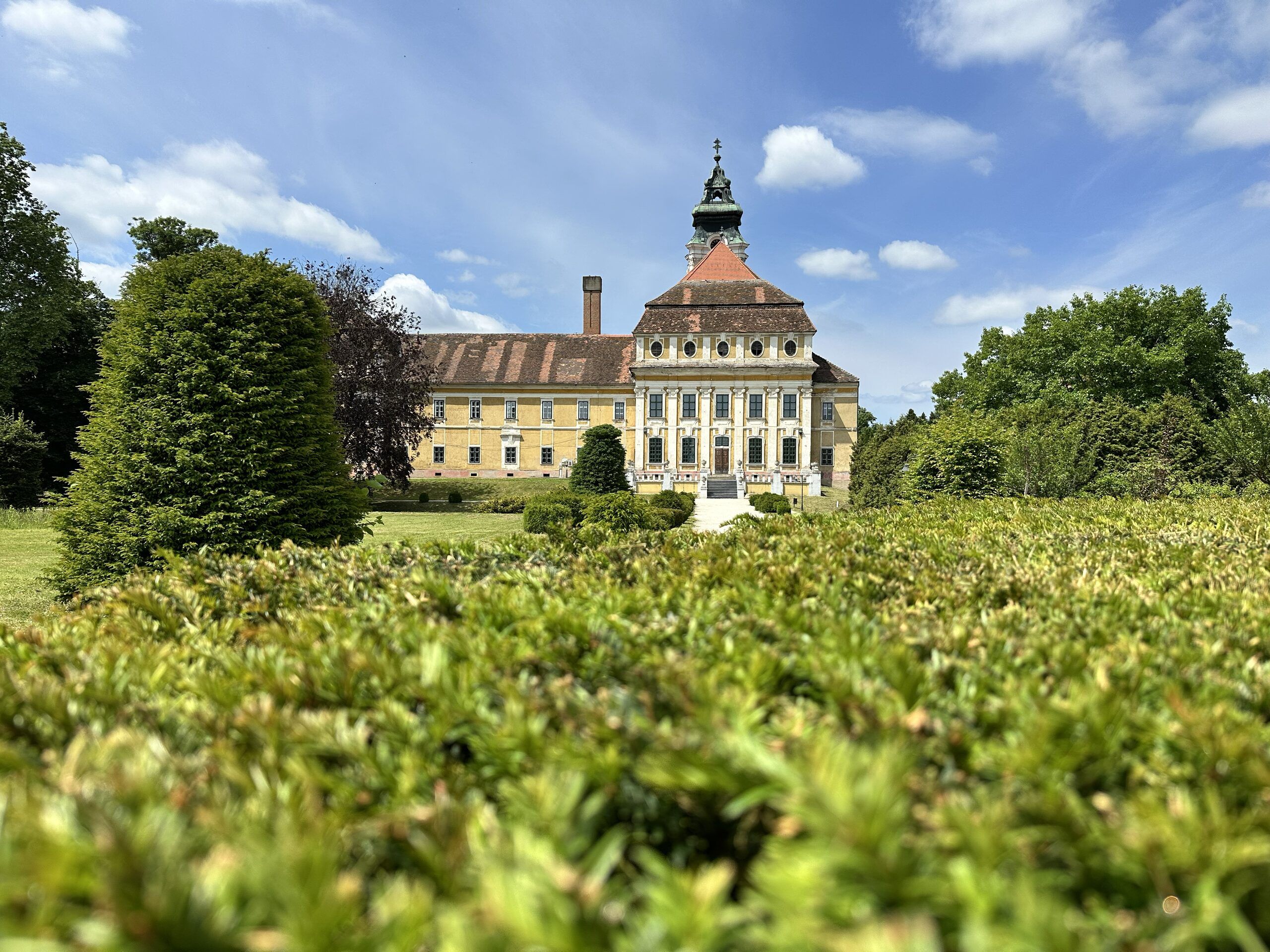 The yellow baroque facade of the Cistercian abbey in Szentgotthárd behind clipped hedges